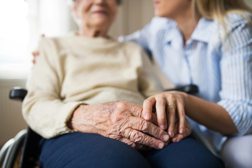 A woman gently holds the hand of an elderly woman, conveying support and connection between them.