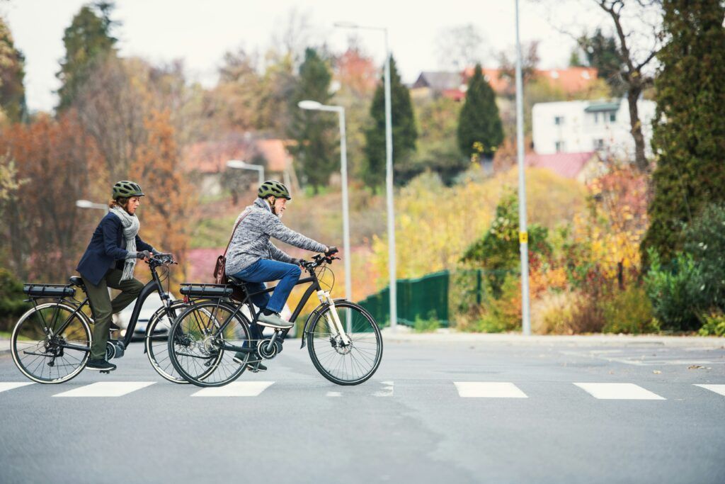 Two people riding bicycles side by side on a city street, surrounded by trees and buildings.