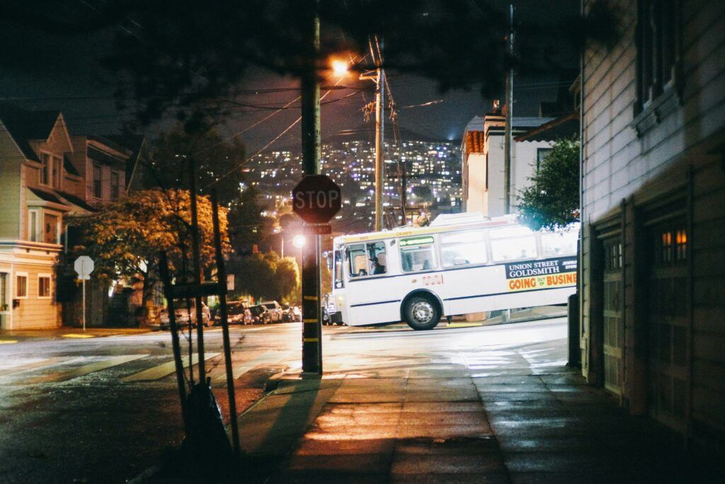 A bus driving down a dimly lit street at night, with streetlights illuminating the surroundings.