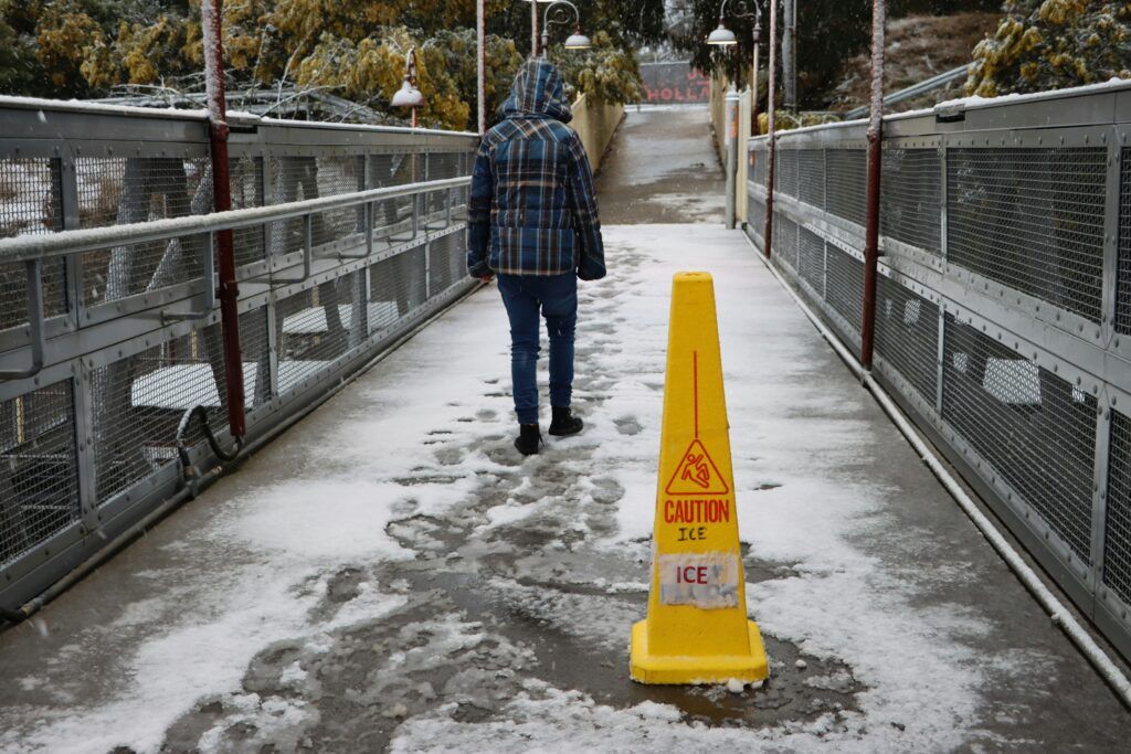 A person walks on a bridge beside a yellow caution cone, indicating a potential hazard in the area.