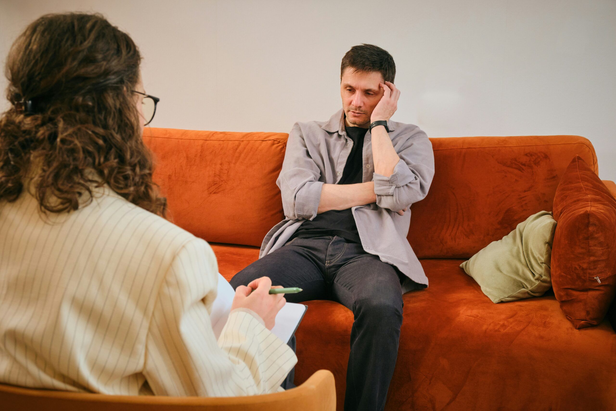 A man and a woman sit together on an orange couch, engaged in conversation.