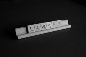 Black-and-white image of wooden letter tiles spelling “LAWYER” arranged on a small wooden holder against a dark background, with soft lighting creating a professional and minimalist legal theme.