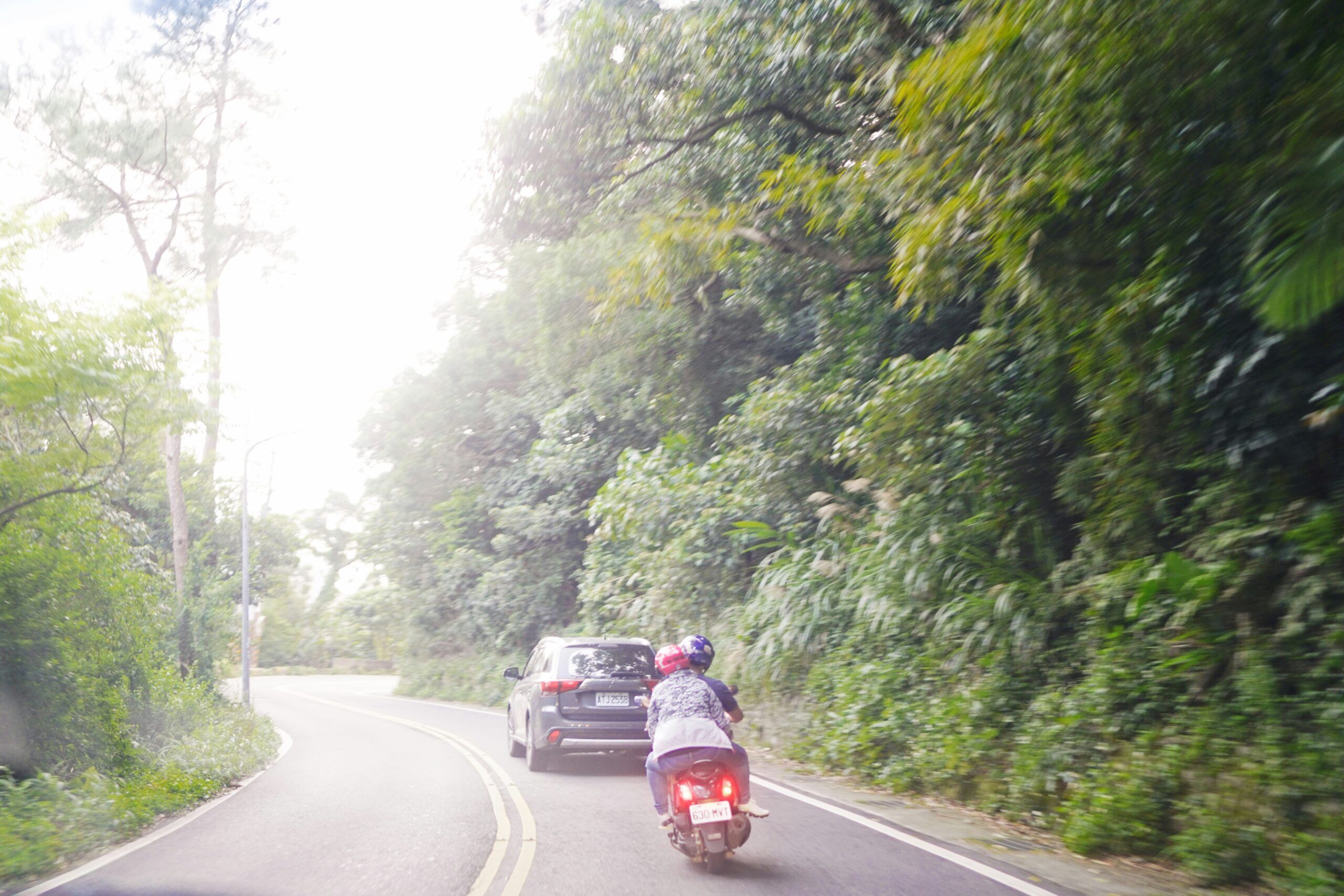 A person riding a motorcycle along a winding road surrounded by trees and open fields.