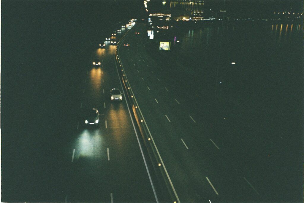 A nighttime highway scene with cars driving, illuminated by streetlights and headlights.
