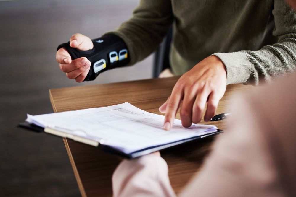 A man wearing a wrist brace consults with a woman holding a pen, discussing personal injury legal matters.